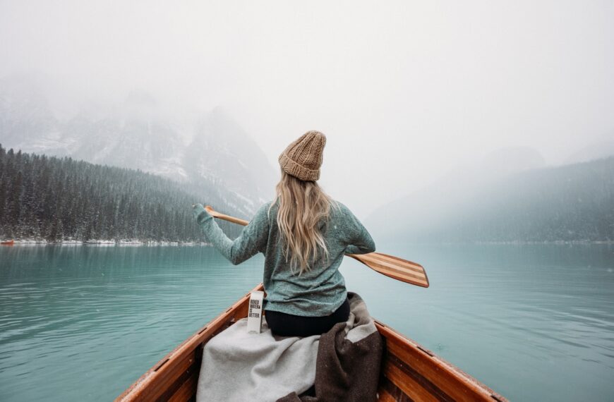 woman in gray long sleeve shirt sitting on brown wooden boat on body of water during