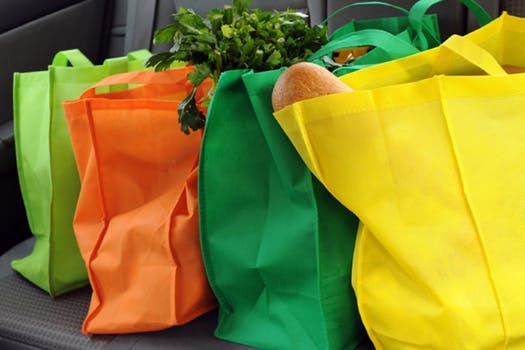 Four reusable grocery bags next to each other with groceries inside 