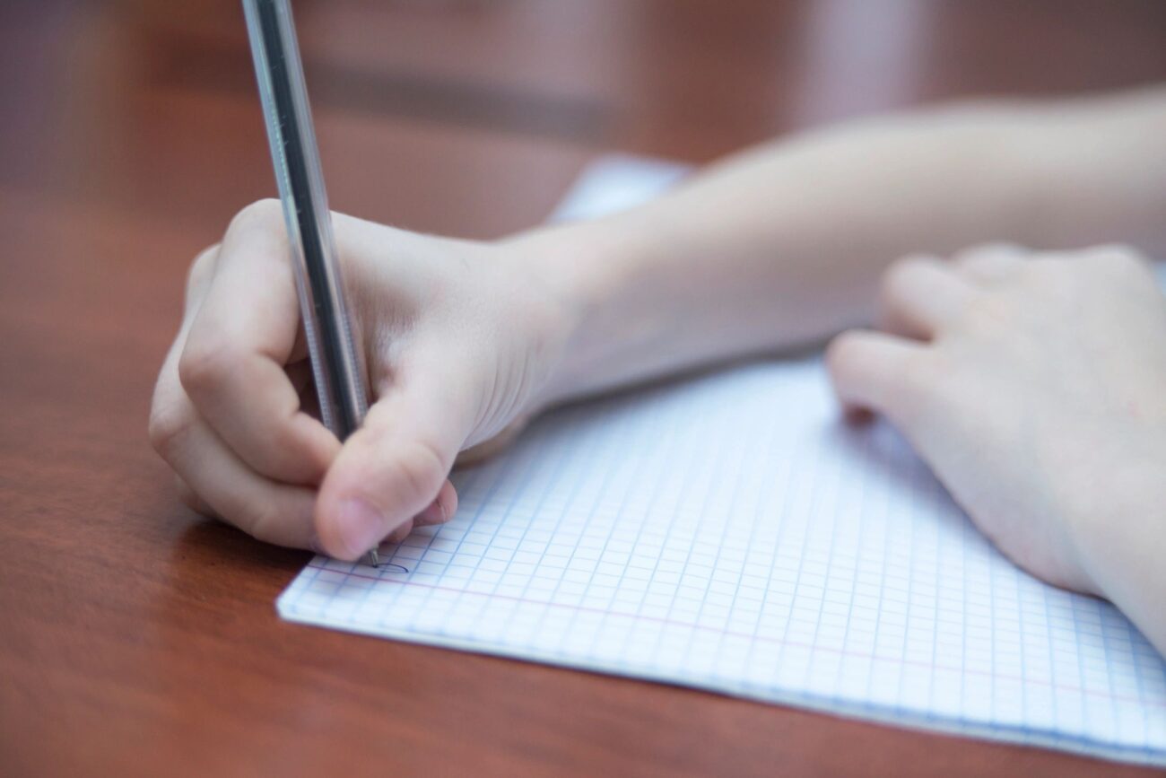 College student overcoming procrastination by starting to write on a piece of paper on a wooden desk.